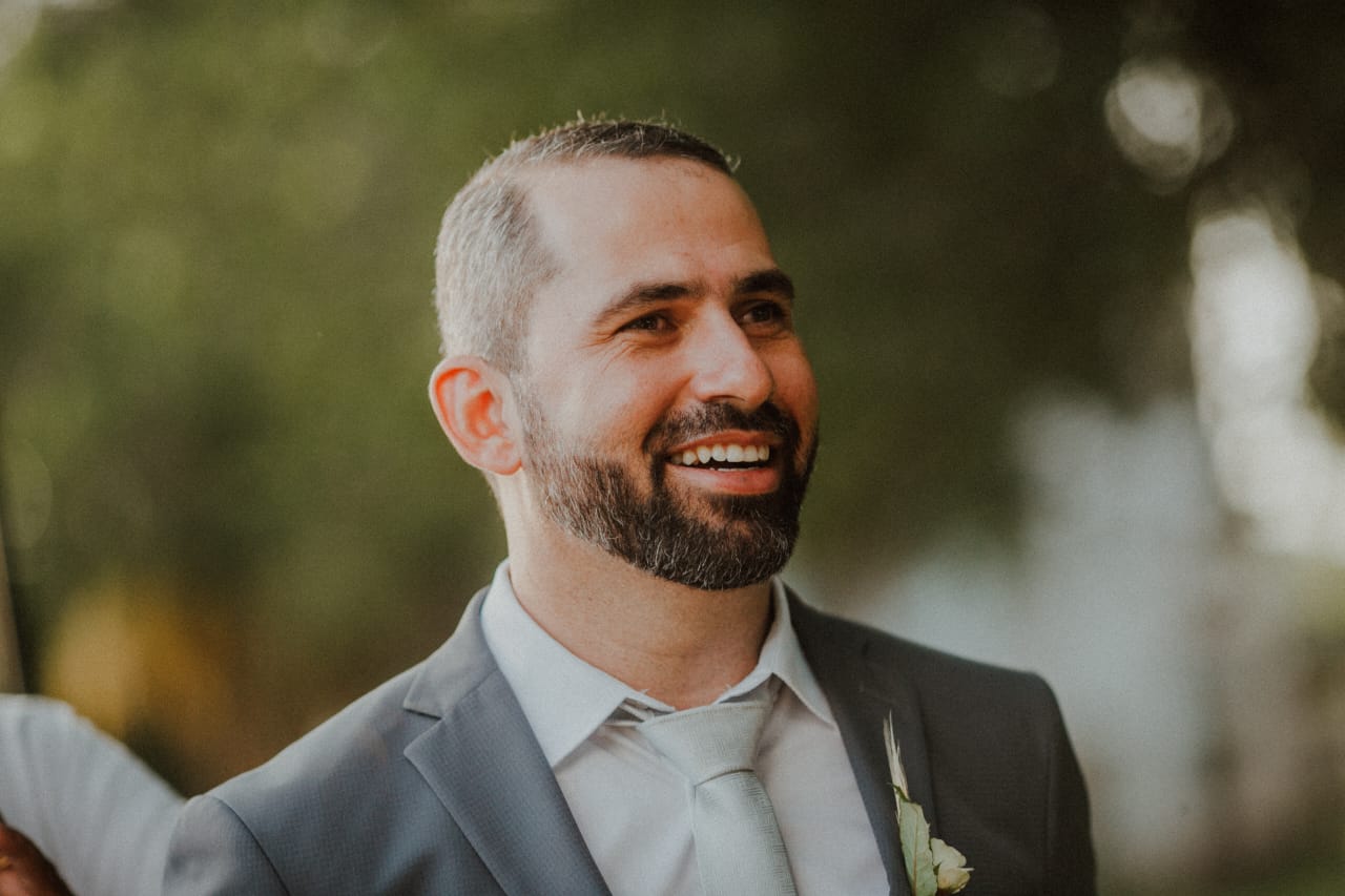 Imagem de Ronny vestindo palitó sorrindo com plantas no fundo